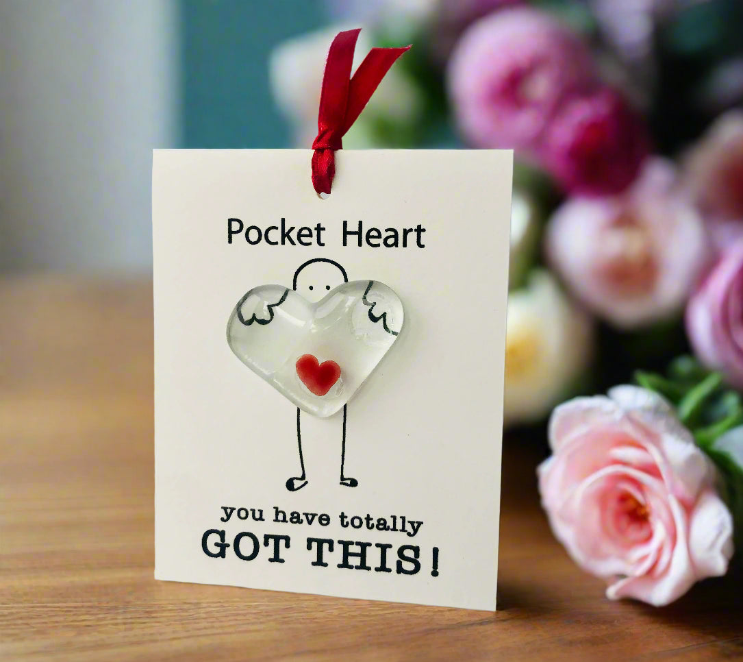 Heart-shaped pocket charm with a red ribbon on a white card with text